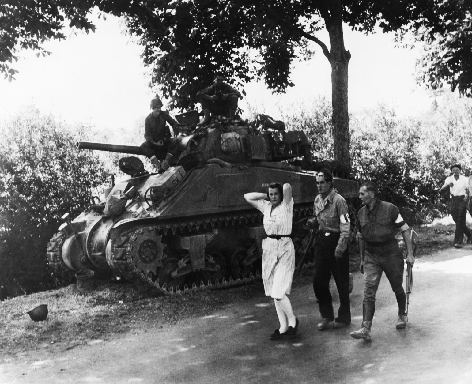 A French woman, accused of being a German sympathizer, is marched along a road past an American heavy tank followed by two armed French partisans on August 19, 1944. She is being taken to Pre en Pail, France, there to be shorn of her hair. (AP Photo)