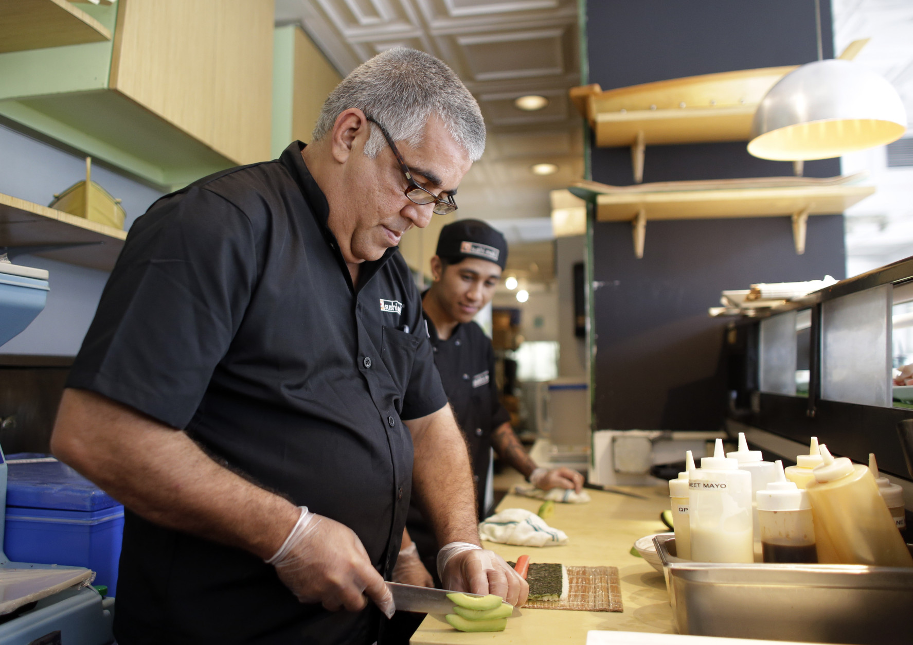 Chef Lucio Alfonso Perez, of Cuba, left, slices avocado for a sushi roll as he works with Kenneth Oliveros, right, at a Sushi Maki restaurant, Wednesday, Aug. 12, 2015, in Miami. Perez is one of four Cuban chefs visiting Miami for the week as part of the chef exchange program being hosted by the Cuba Study Group. The initiative is meant to encourage collaboration and development of new skills. Perez is the chef at Gringo Viejo, which serves traditional Cuban cuisine, and Cuban fusion, in Havana. (AP Photo/Lynne Sladky)