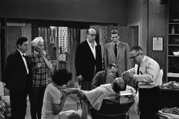 Rehearsing an episode for the series, Dick Van Dyke, right, and three other regulars in the show gather around Carl Reiner, who plays the part of their boss, in barber chair, April 11, 1963.  Standing from left; Morey Amsterdam, Rose Marie, and Richard Deacon. The rest of the group is unidentified. Reiner also produces and writes the series. As the TV score is added up to see which shows will be back next fall, The Dick Van Dyke Show is found among the survivors. The comedy series on CBS-TV will go on while a number of Western and anthology type shows are being dropped. (AP Photo/David F. Smith)