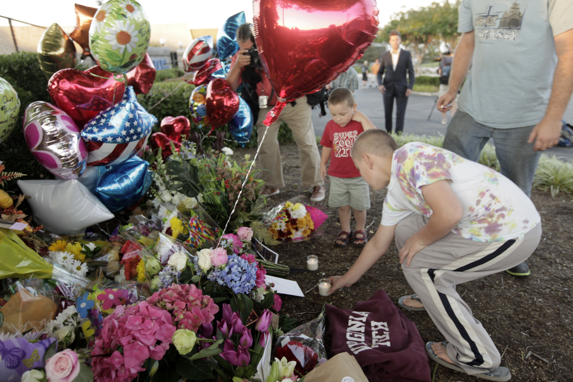 ROANOKE, VA - AUGUST 26: Jason and Patricia Grice and their sons Matthew Fajardo, 11, and William , 3, (background) bring flowers and candles to a memorial for the two journalists that were killed this morning during a live broadcast on August 26, 2015 in Roanoke, Virginia. Two employees of WDBJ TV were killed this morning during a live broadcast at Bridgewater Plaza on Smith Mountain Lake. The victims have been identified as reporter Alison Parker and cameraman Adam Ward. Parker, 24 and Ward, 27, worked for WDBJ in Roanoke, Virginia. The suspect, Vester Lee Flanigan, also known as Bryce Williams, died of a self-inflicted gunshot wound. (Photo by Jay Paul/Getty Images)