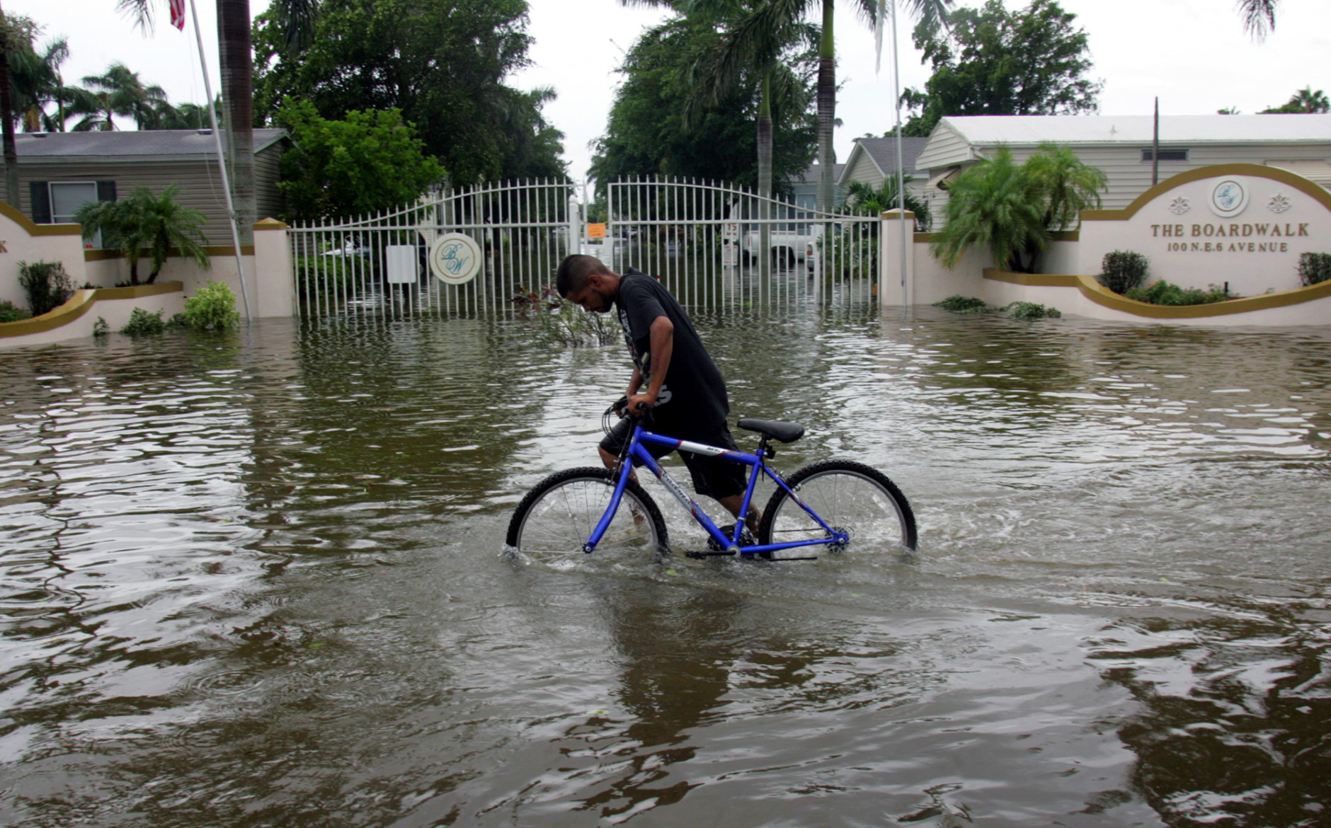 Noe Morua pushes his bike past a flooded mobile home park in Homestead, Fla., Friday, Aug. 26, 2005. Hurricane Katrina flooded streets, darkened homes and felled trees as it plowed across South Florida before emerging over the Gulf of Mexico. (AP Photo/Luis M. Alvarez)