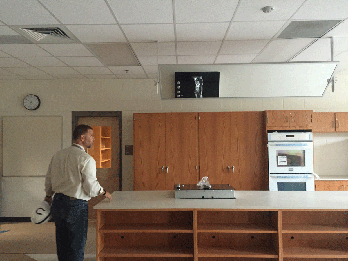 Principal looking at the teacher's station in the gourmet food classroom. The miror above the island allows students to get a clearer view of what the teacher is demonstrating. (WTOP/Max Smith)