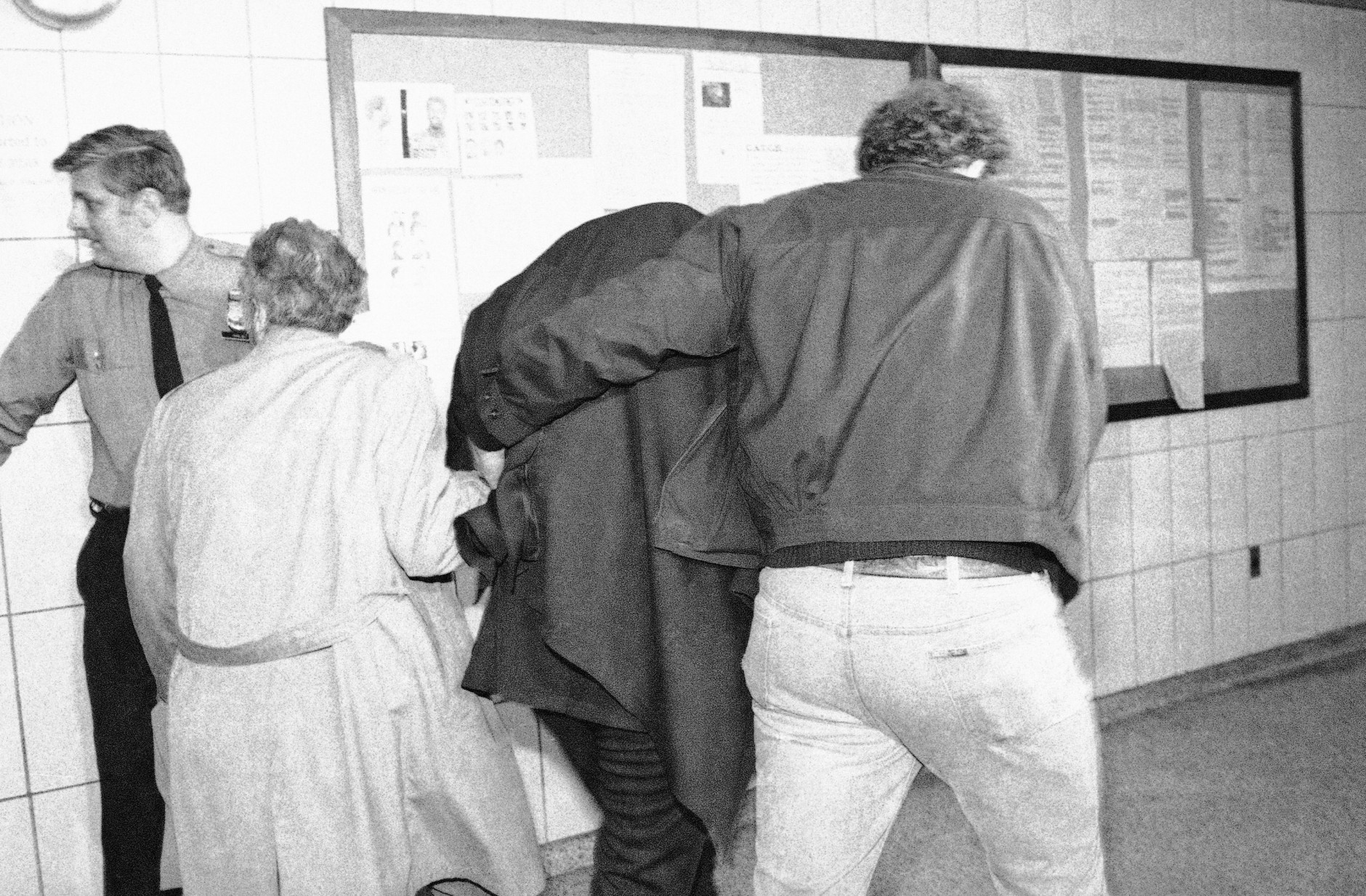 A man believed to be Mark David Chapman, covered center, is hustled from a New York City police station, to be booked at headquarters, Tuesday, Dec. 9, 1980. Chapman is expected to be charged in the murder of former Beatle John Lennon in New York last night. (AP Photo/Handshuh)