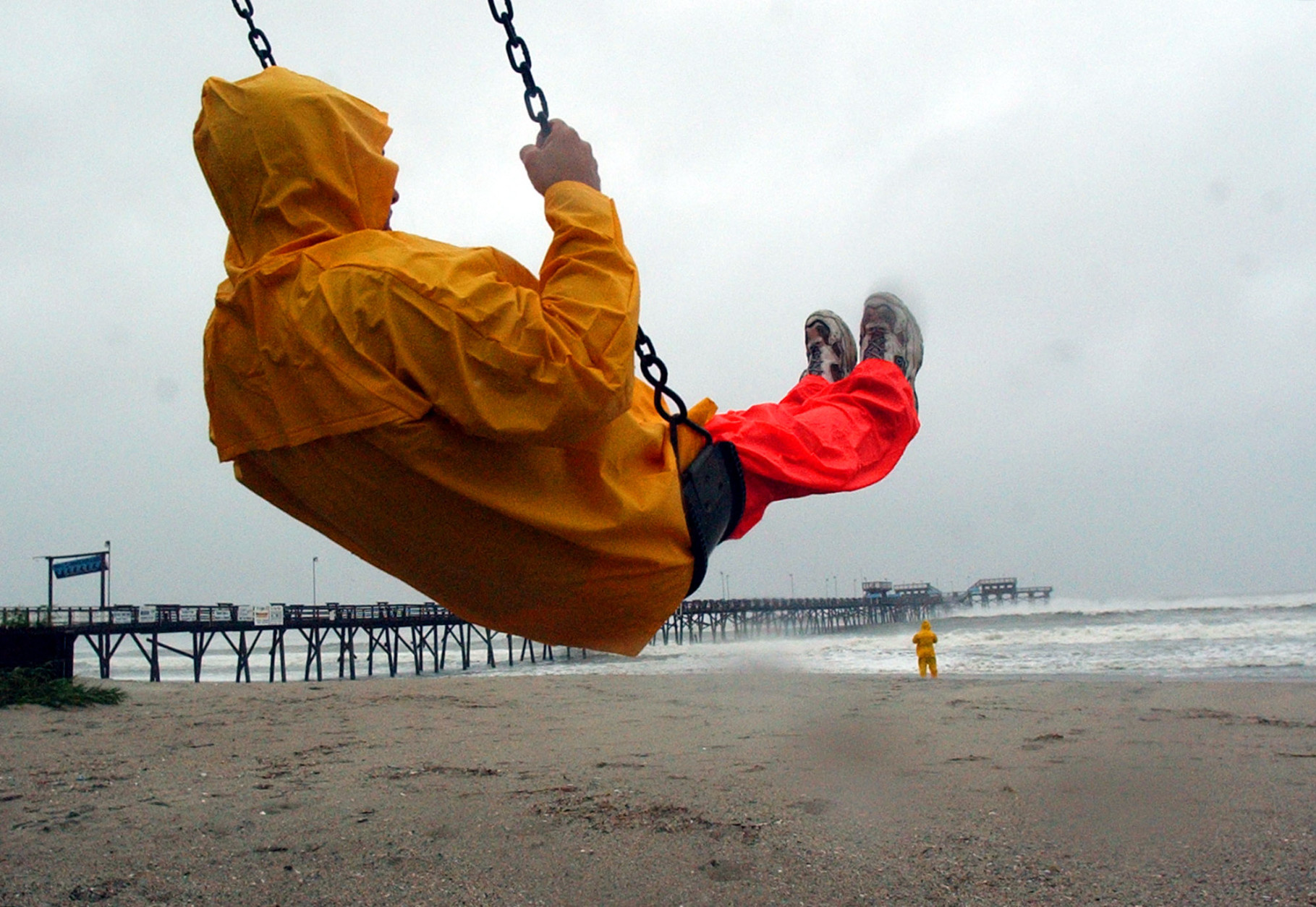 Jack Pierce, 38, of High Point, NC., takes a moment to swing on a playground set next to the Triple S Pier in Atlantic Beach, N.C., on Thursday, Sept. 18, 2003. At rear his brother Scott, 32, walks along the beach and watches the waves crash against the pier as Hurricane Isabel approaches landfall. (AP Photo/Dave Martin)