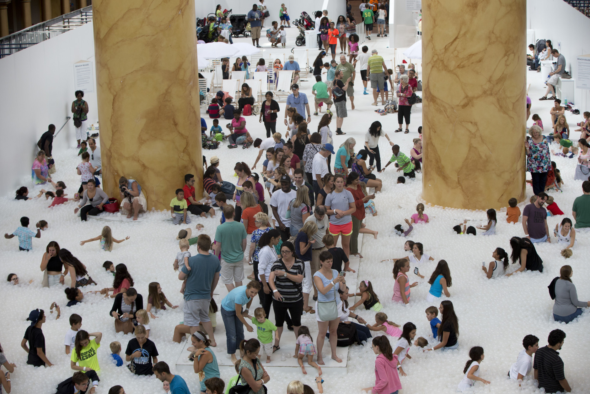 Children and adults play at "The Beach", an interactive architectural installation inside the National Building Museum in Washington, Wednesday, July 29, 2015. The Beach, which spans the length of the museum's Great Hall, was created in partnership with Snarkitecture, and covers 10,000 square feet and includes an ocean of nearly one million recyclable translucent plastic balls.   (AP Photo/Carolyn Kaster)