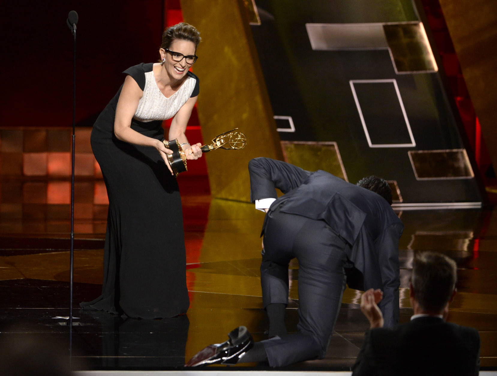 Jon Hamm crawls on stage to accept the award from Tina Fey for outstanding lead actor in a drama series for Mad Men at the 67th Primetime Emmy Awards on Sunday, Sept. 20, 2015, at the Microsoft Theater in Los Angeles. (Photo by Phil McCarten/Invision for the Television Academy/AP Images)