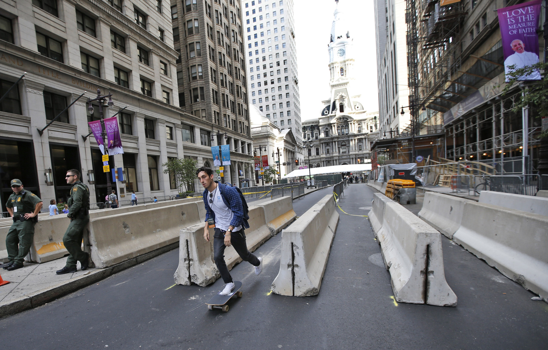 A man on a skateboard rides through a security checkpoint on Broad Street with City Hall in the background in Philadelphia on Friday, Sept. 25, 2015, before Pope Francis' upcoming visit. (AP Photo/Alex Brandon)