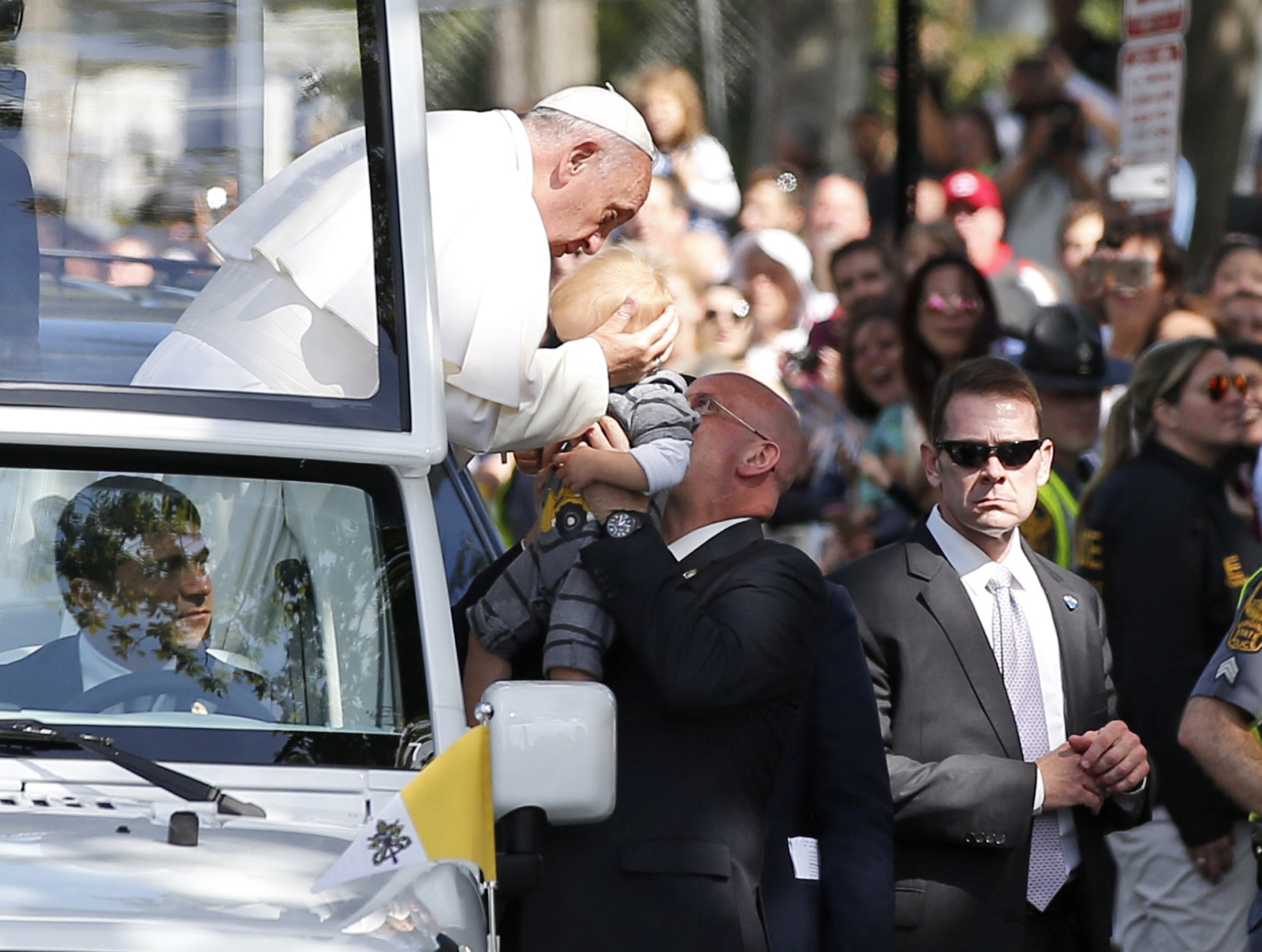 Pope Francis holds the head of a small child as he leans from the popemobile during a parade, Wednesday, Sept. 23, 2015, in Washington. (AP Photo/Alex Brandon, Pool)