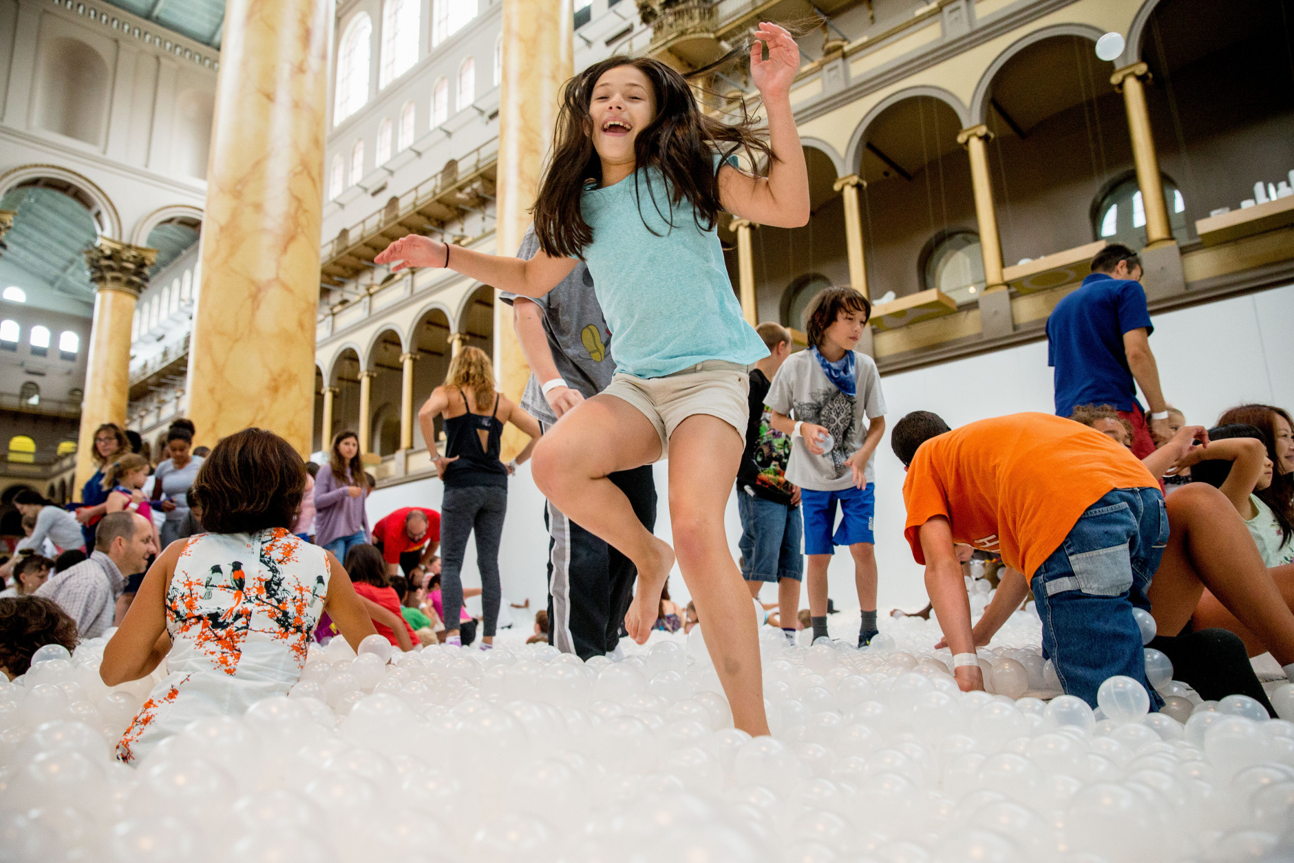Ilana Cohen, 9, of Alexandria, Va., jumps into a sea of plastic balls at "The Beach", an interactive architectural installation inside the National Building Museum in Washington, Friday, July 17, 2015. The Beach, which spans the length of the museum's Great Hall, was created in partnership with Snarkitecture, and covers 10,000 square feet and includes an ocean of nearly one million recyclable translucent plastic balls. (AP Photo/Andrew Harnik)