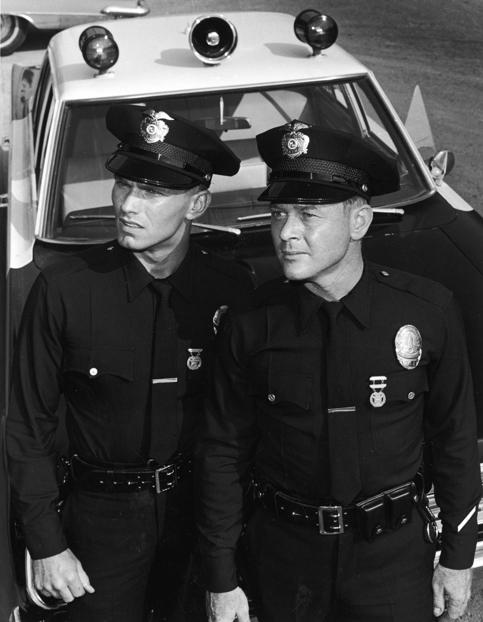 Actors Martin Milner (right) and Kent McCord stand in uniform by their patrol car in a promotional still for the television series, 'Adam 12,' c. 1969. (Photo by NBC Television/Courtesy of Getty Images)