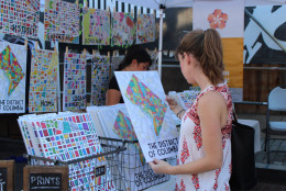 A festivalgoer checks out an illustrated poster at one of the stalls on H Street. (WTOP/Dana Gooley)