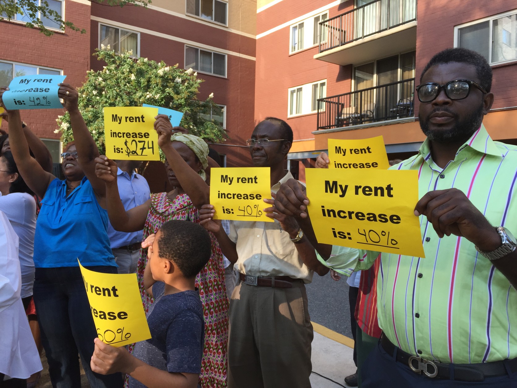 At a press conference Monday night, residents of the Hampshire Tower Apartments held up signs showing the big rent increases they're facing.  (WTOP/Michelle Basch)