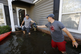 Jan-Patrick Gros, left, hands his good Ethan Abbott his sandals after Abbott helped Gros get personal item out of Gros' house to get it out of floodwaters in the Ashborough subdivision near Summerville, S.C., Tuesday, Oct. 6, 2015. Residents are concerned that the Ashley river will continue to rise as floodwaters come down from Columbia.  (AP Photo/Mic Smith)