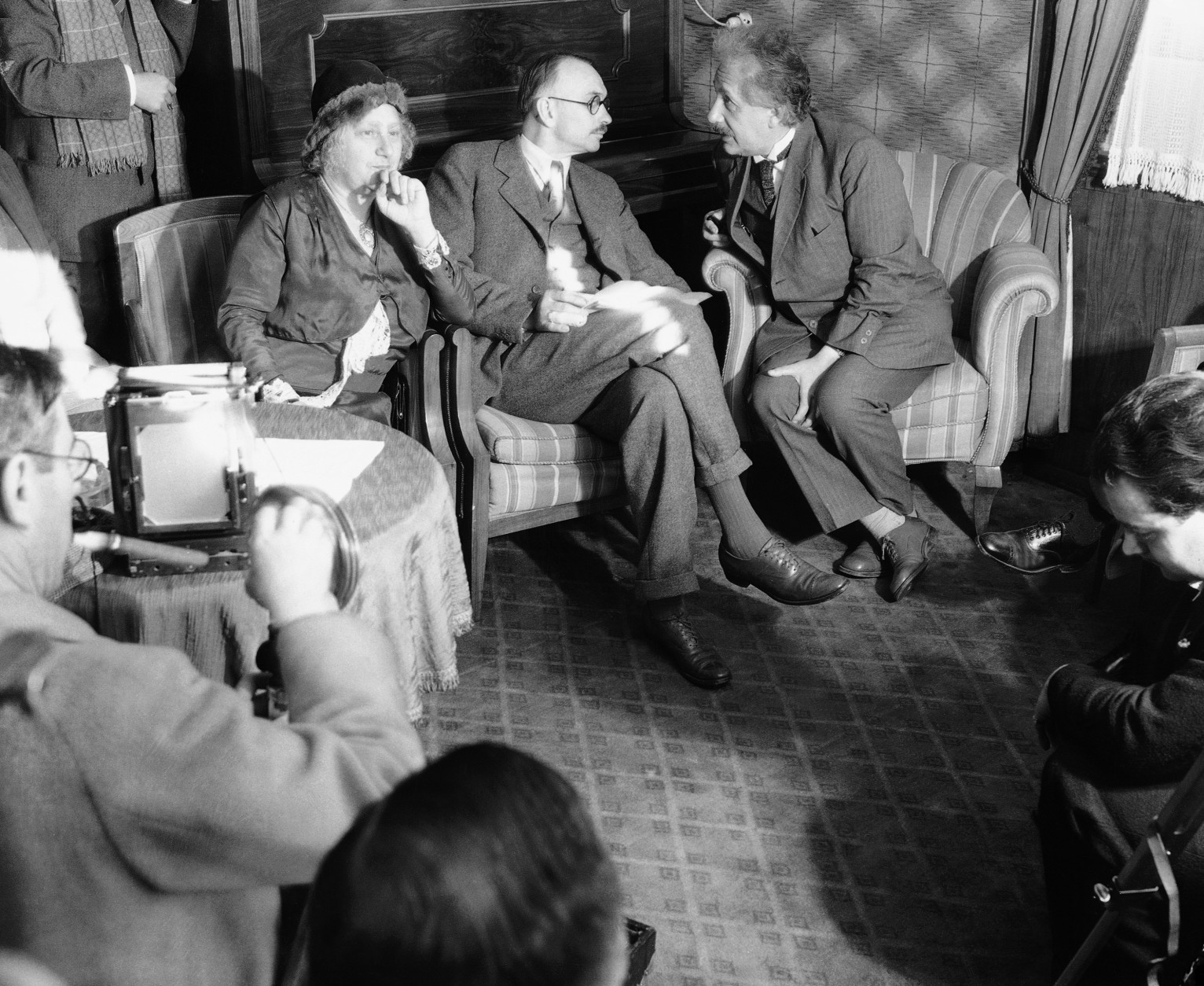 Some of the questions were pretty hard to answer and others were amusing, but Dr. Albert Einstein, noted physicist, right, did his best to enlighten newspaper reporters who met him on his arrival aboard the motor ship Portland in Los Angeles, Calif., Dec. 30, 1932.  Dr. R.C. Tolman, of the California Institute of Technology, center, is who put the newsmen's questions to Dr. Einstein. Einstein's wife Elsa is at the left. (AP Photo)