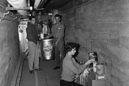 Students at National College in Kansas City begin stocking a tunnel under the campus with survival supplies shown Oct. 24, 1962. College officials said it was a precautionary measure against possible atomic attack. Irene Peters, 19, Canton, Mo., stacks canned goods. In background, Edgar Walden, left, Indianapolis, and Jim Potter, Kansas City, carry in water. The college is putting in a two-week supply of food, water and oxygen in two tunnels that connect the building. The school is a Methodist four-year college. (AP Photo/William P. Straeter)