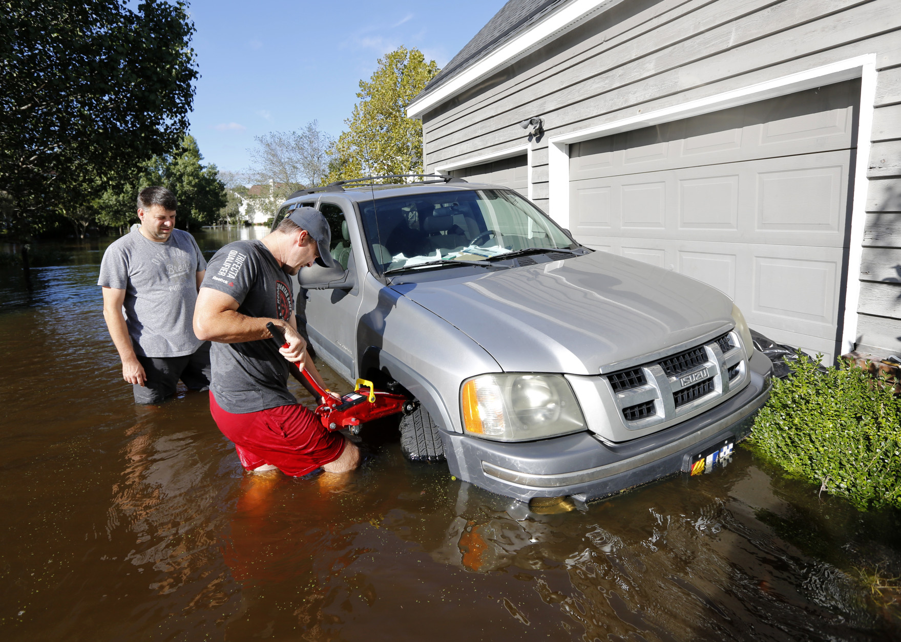 Ethan Abbott, at right, helps friend, Jan-Patrick Gros try to jack up Gros' vehicle to get it out of floodwaters in the Ashborough subdivision near Summerville, S.C., Tuesday, Oct. 6, 2015. Residents are concerned that the Ashley river will continue to rise as floodwaters come down from Columbia.  (AP Photo/Mic Smith)