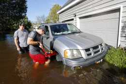 Ethan Abbott, at right, helps friend, Jan-Patrick Gros try to jack up Gros' vehicle to get it out of floodwaters in the Ashborough subdivision near Summerville, S.C., Tuesday, Oct. 6, 2015. Residents are concerned that the Ashley river will continue to rise as floodwaters come down from Columbia.  (AP Photo/Mic Smith)
