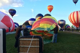 A balloon is filled in the foreground while others launch behind it. (WTOP/Noah Frank)