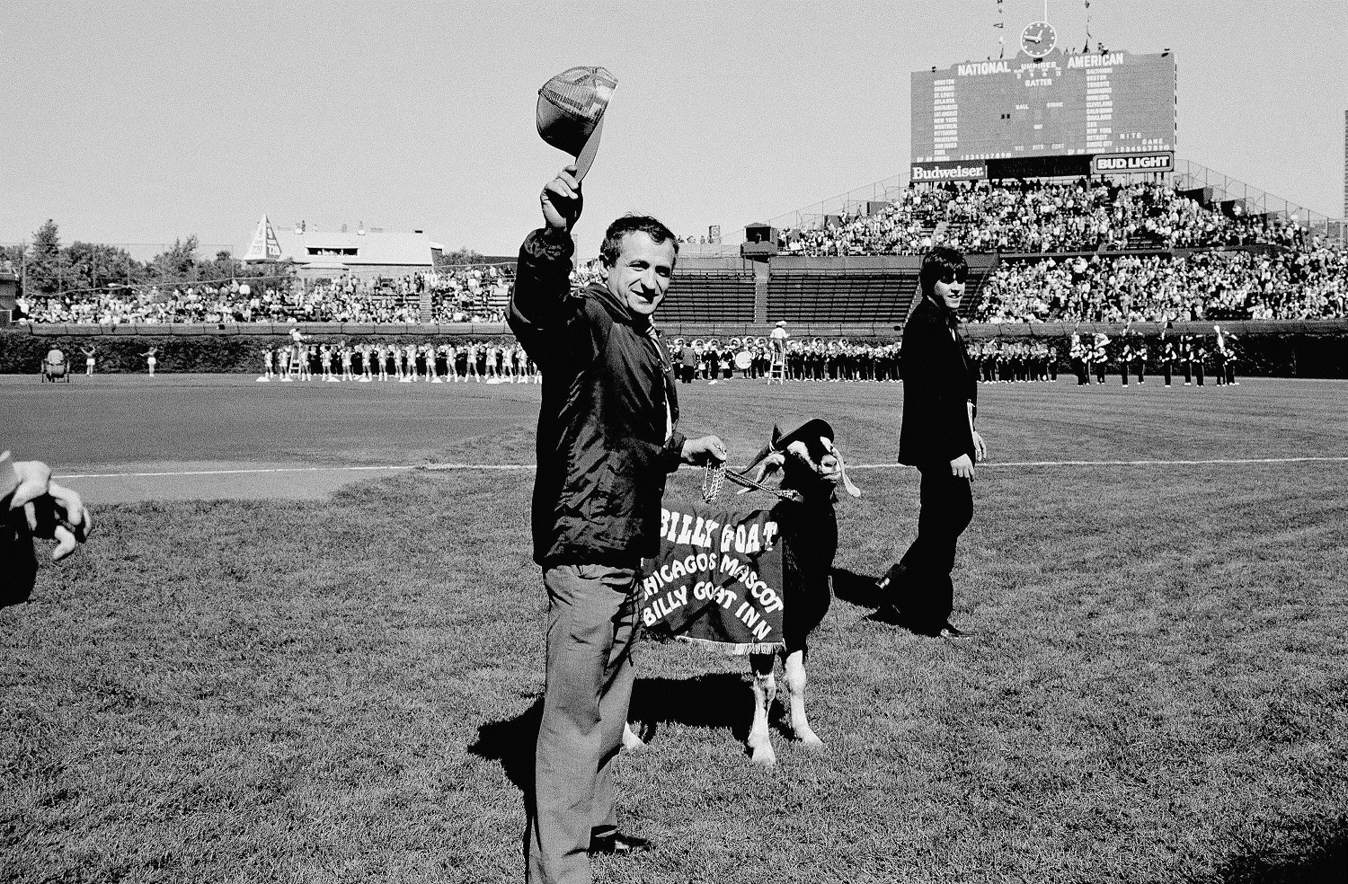 Sam Sianis, owner of the Billy Goat Tavern in Chicago, center, acknowledges the crowd along with his goat prior to the start of the National League playoff game between the Padres and the Cubs, Tuesday, Oct. 2, 1984, Chicago, Ill. Sianis and the goat were invited as guests of the Cubs, both begin issued tickets. The man on the right is unidentified. (AP Photo)