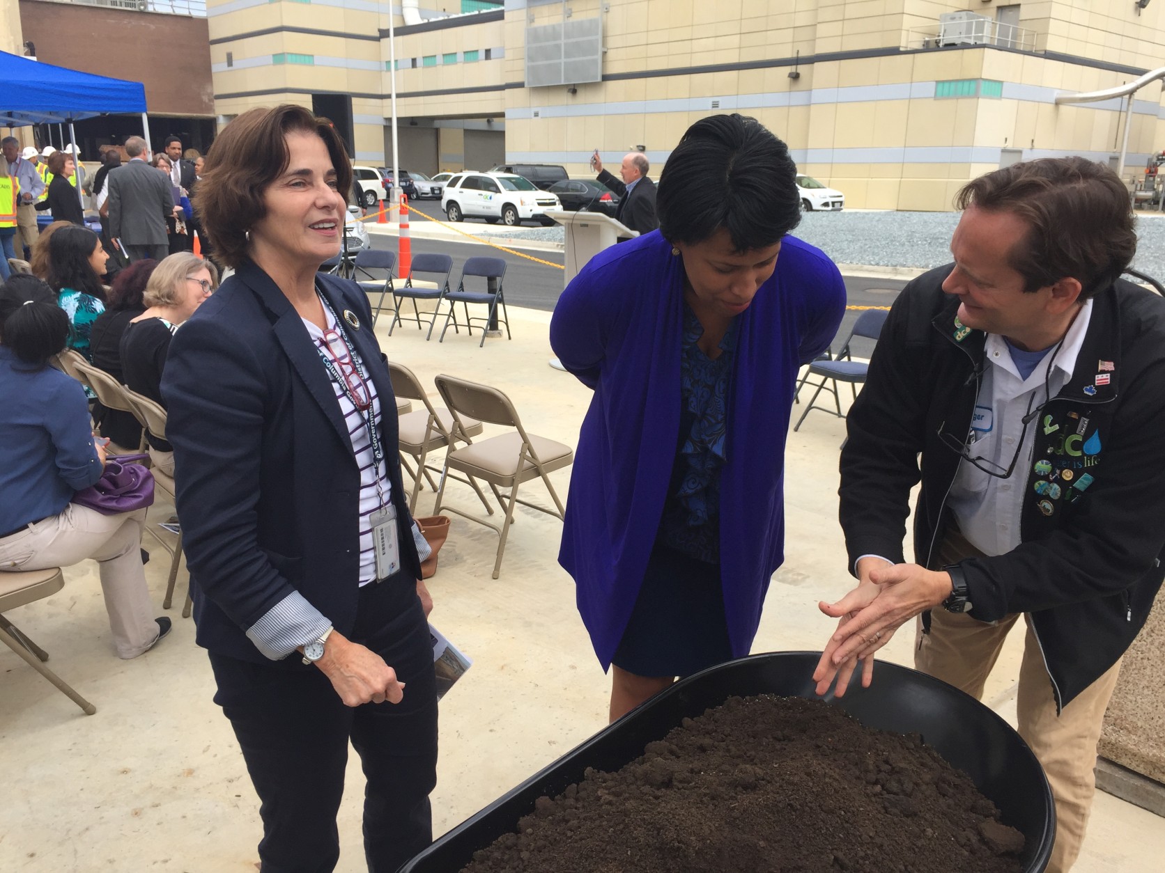 George Hawkins, right, shows Mayor Muriel Bowser the remaining compost-like material, as council member Mary Cheh looks on. (WTOP/Andrew Mollenbeck)