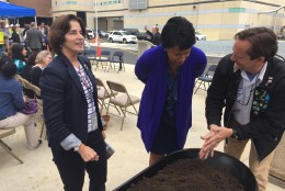 George Hawkins, right, shows Mayor Muriel Bowser the remaining compost-like material, as council member Mary Cheh looks on. (WTOP/Andrew Mollenbeck)