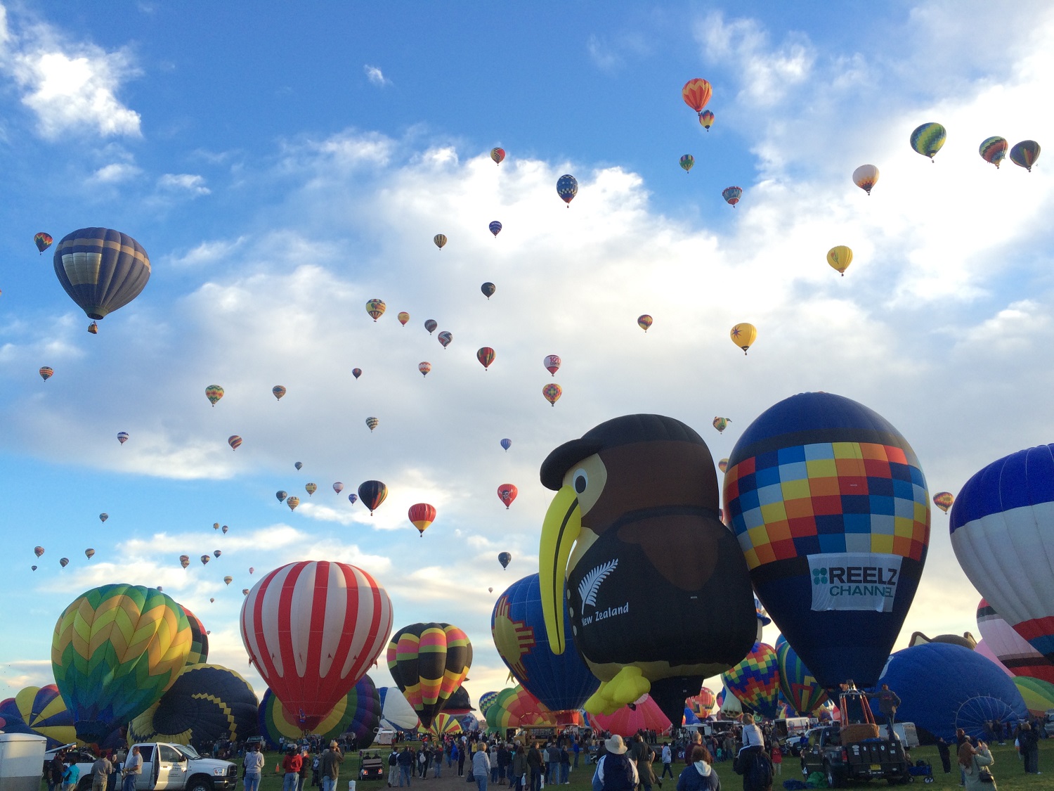 A kiwi balloon inflates in the foreground while dozens of others fly behind it. (Not all balloons take the traditional shape. There were ones shaped like cows, fire hydrants, Darth Vader's helmet, and these cartoon animal characters. (WTOP/Noah Frank)