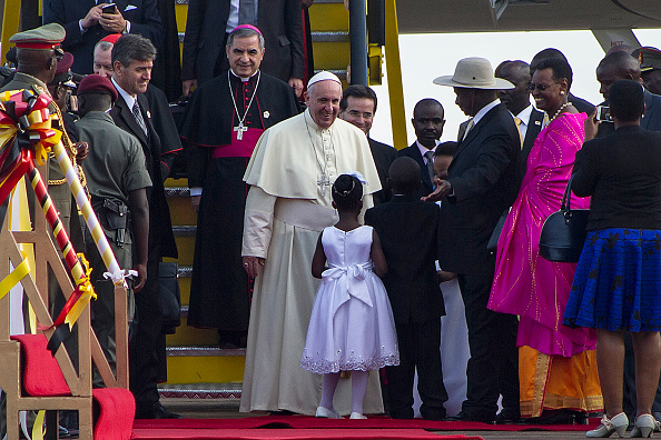 Pope Francis (C) is greeted a young girl and Uganda President Yoweri Museveni (3-R), upon his arrival on November 27, 2015 in Entebbe. Pope Francis arrived in Uganda on November 27 on the second leg of a landmark trip to Africa which has seen him railing against corruption and poverty, with huge crowds celebrating his arrival. AFP PHOTO / ISAAC KASAMANI / AFP / ISAAC KASAMANI        (Photo credit should read ISAAC KASAMANI/AFP/Getty Images)