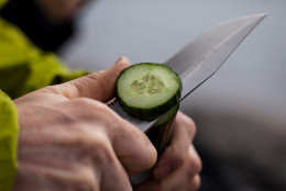 Cropped hands of man cutting cucumber outdoors