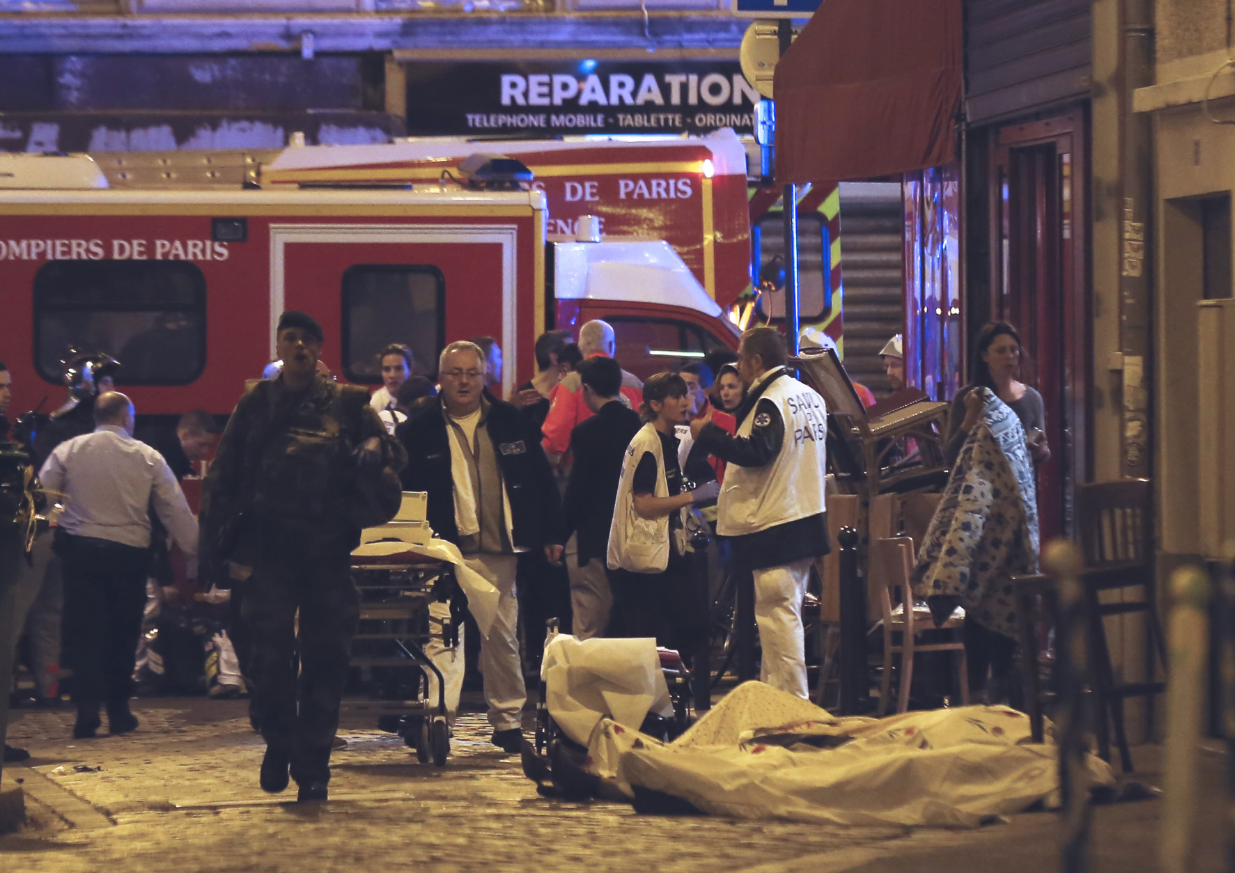 Police officers and rescue workers gather around a victim outside in the 10th district of Paris, Friday, Nov. 13, 2015.  At least 35 people were killed Friday in shootings and explosions around Paris, many of them in a popular concert hall where patrons were taken hostage, police and medical officials said. (AP Photo/Jacques Brinon)