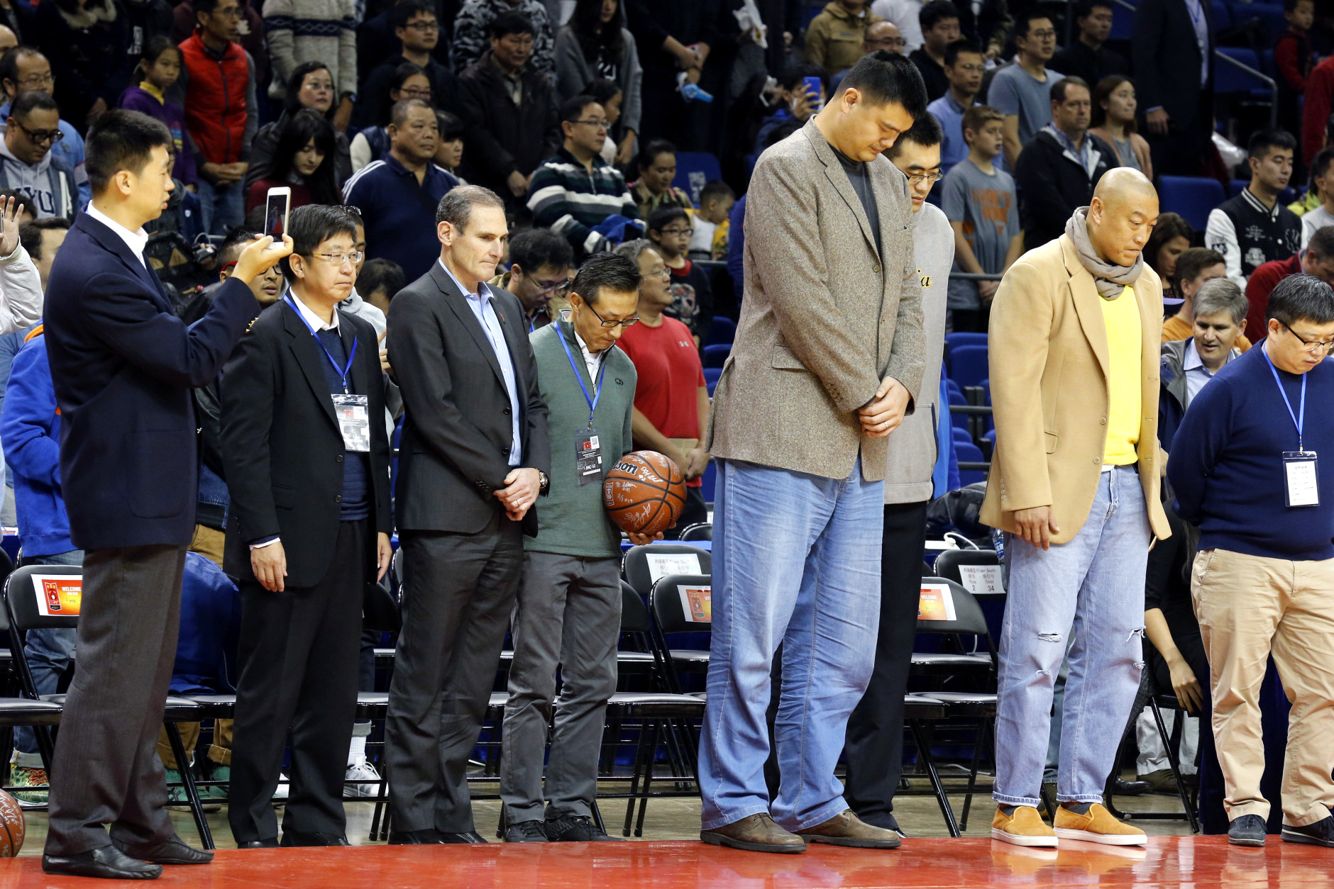 Former NBA star Yao Ming, third from right bows as he observes a moment of silence with other attendees to mark the terror attacks in Paris before a college basketball match between Washington Huskies and Texas Longhorns at the Mercedes Benz Arena in Shanghai, China, Saturday, Nov. 14, 2015. (AP Photo/Ng Han Guan)
