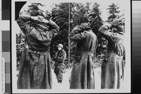 US soldier aiming his rifle at captured Nazi prisoners, who have hands on top of heads in surrender in snowy landscape, during Battle of Bulge.  (Photo by Time Life Pictures/Office Of War Information/National Archives/The LIFE Picture Collection/Getty Images)