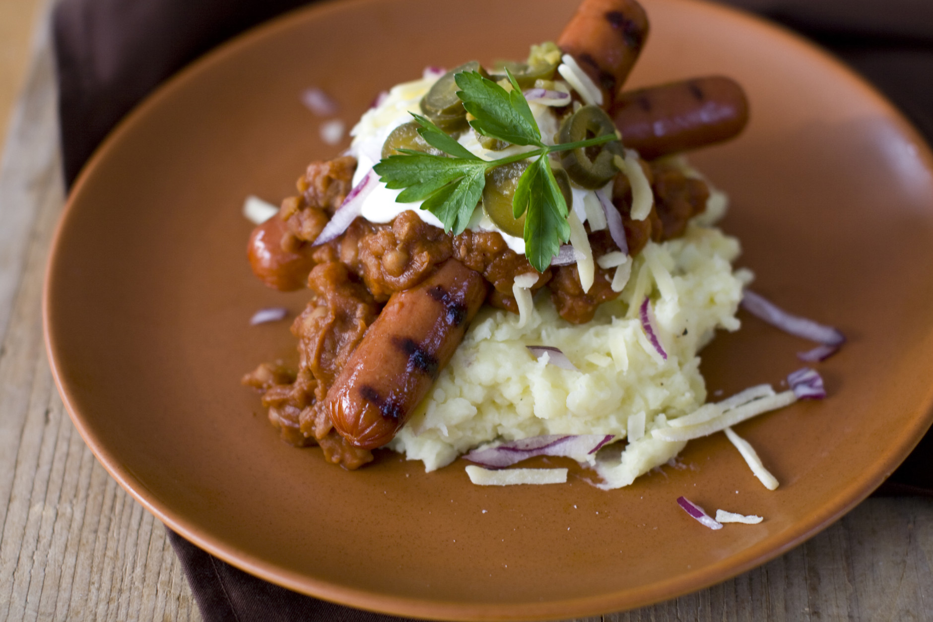 This Oct. 31, 2011 photo shows winter chili dogs in Concord, N.H.  To serve, divide the mashed potatoes between 4 serving plates. Top each with a hot dog, then ladle the beans over them. Top with cheese, sour cream, jalapenos and red onion.    (AP Photo/Matthew Mead)