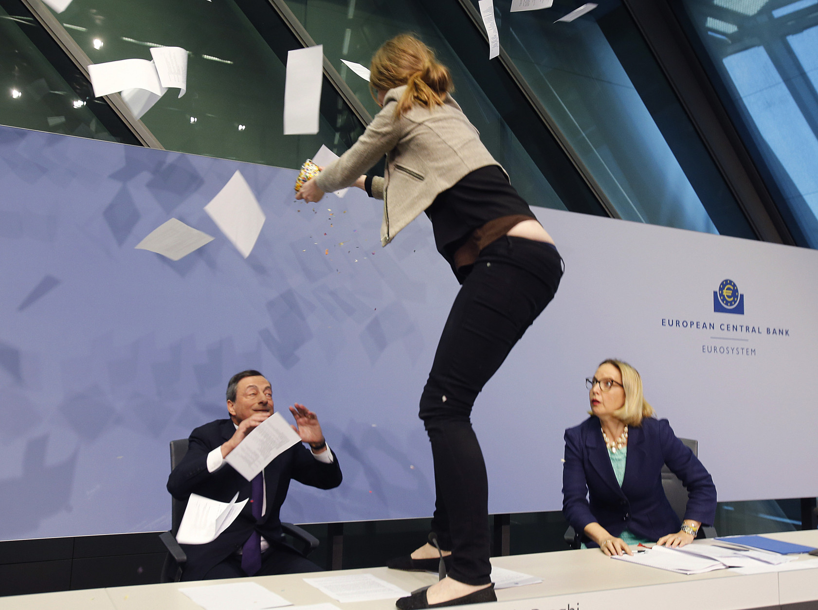 FOR USE AS DESIRED, YEAR END PHOTOS - FILE - An activist stands on the table of the podium throwing paper at ECB President Mario Draghi, left, as Christine Graeff, Director General of Communications, looks on during a press conference of the European Central Bank, ECB, in Frankfurt, Germany, Wednesday, April 15, 2015. (AP Photo/Michael Probst, File)