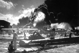 In this image provided by the U.S. Navy, sailors stand among wrecked airplanes at Ford Island Naval Air Station as they watch the explosion of the USS Shaw in the background, during the Japanese surprise attack on Pearl Harbor, Hawaii, on December 7, 1941. (AP Photo/U.S. Navy)