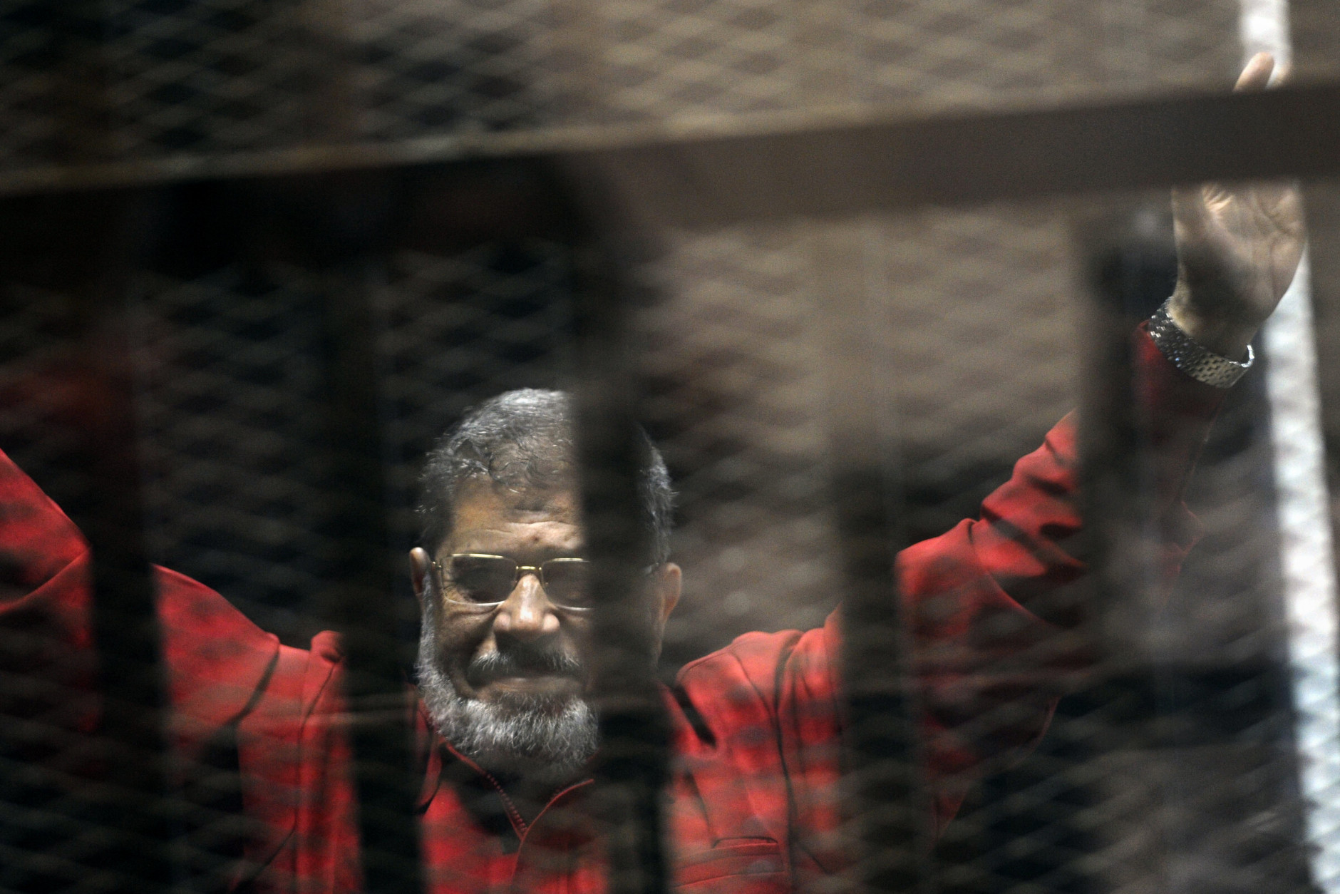 FOR USE AS DESIRED, YEAR END PHOTOS - FILE - Ousted Egyptian President Mohammed Morsi, wearing a red jumpsuit that designates he has been sentenced to death, raises his hands inside a defendants cage in a makeshift courtroom at the national police academy, in an eastern suburb of Cairo, Egypt, Sunday, June 21, 2015. The week before, a court sentenced Morsi to death in a separate case over a prison break in 2011. (AP Photo/Ahmed Omar, File)