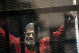 FOR USE AS DESIRED, YEAR END PHOTOS - FILE - Ousted Egyptian President Mohammed Morsi, wearing a red jumpsuit that designates he has been sentenced to death, raises his hands inside a defendants cage in a makeshift courtroom at the national police academy, in an eastern suburb of Cairo, Egypt, Sunday, June 21, 2015. The week before, a court sentenced Morsi to death in a separate case over a prison break in 2011. (AP Photo/Ahmed Omar, File)