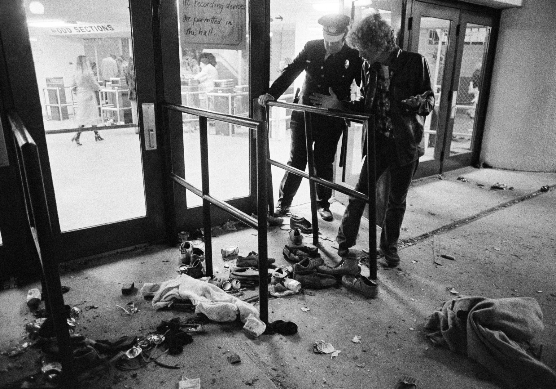 A security guard and an unidentified man look at an area where several people were killed as they were caught in a surging crowd entering Cincinnati's Riverfront Coliseum for a Who concert on Monday. Shoes and clothes were strewn around the area where the people were killed and injured, shown Dec. 4, 1979. (AP Photo/Brian Horton)