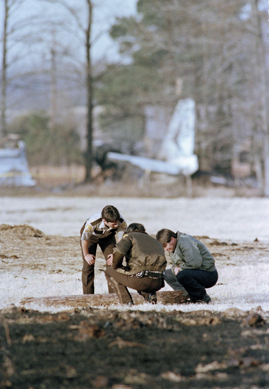 Airplane part in background marks the area where Ricky Nelson's private plane crashed on New Years Eve, in De Kalb, northeast of Dallas, Texas. Seven of the nine occupants, including Nelson, were killed in the crash. Unidentified investigators look over the crash site, Jan. 1, 1986.  (AP Photo/Carlos Osorio)