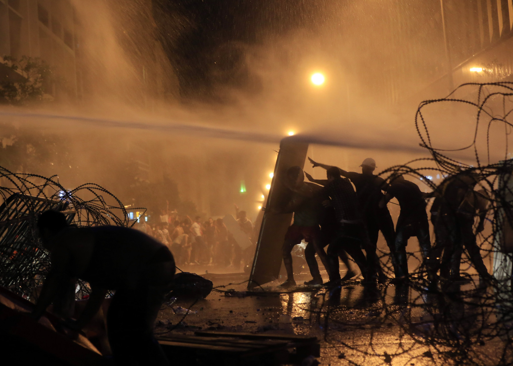 FOR USE AS DESIRED, YEAR END PHOTOS - FILE - Lebanese activists hold up a makeshift shield as they are sprayed by riot police using water cannons during a protest against the ongoing trash crisis, in downtown Beirut, Lebanon, Sunday, Aug. 23, 2015. Lebanese riot police fired several rounds of tear gas and water cannons for the second consecutive day in downtown Beirut as they battled protesters with batons and stones _ a marked escalation of mass demonstrations against an ongoing trash crisis. (AP Photo/Hassan Ammar, File)