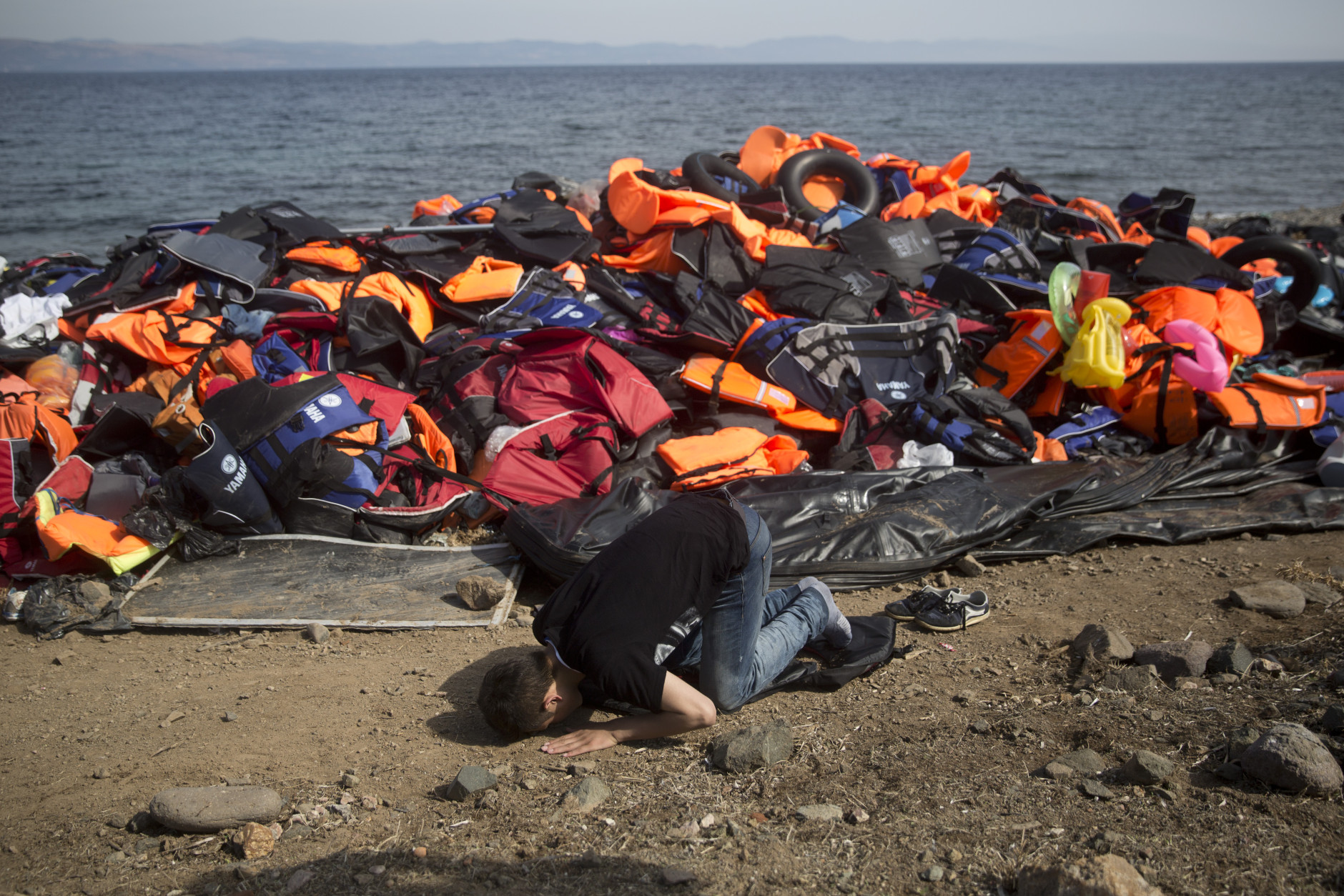 FOR USE AS DESIRED, YEAR END PHOTOS - FILE - An Afghan migrant prays in front a huge pile of life vests after arriving with others from Turkey to the shores of the Greek island of Lesbos, on an inflatable dinghy, Saturday Sept. 26, 2015. More than 260,000 asylum-seekers have arrived in Greece so far this year, most reaching the country's eastern islands on flimsy rafts or boats from the nearby Turkish coast. (AP Photo/Petros Giannakouris, File)