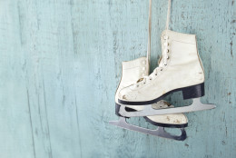 Women's ice skates hanging on blue wooden background