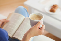 Woman sitting on the sofa reading a book holding her coffee mug