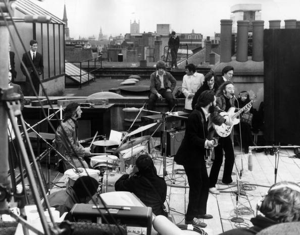 30th January 1969:  British rock group the Beatles performing their last live public concert on the rooftop of the Apple Organization building for director Michael Lindsey-Hogg's film documentary, 'Let It Be,' on Savile Row, London, England. Drummer Ringo Starr sits behind his kit. Singer/songwriters Paul McCartney and John Lennon perform at their microphones, and guitarist George Harrison (1943 - 2001) stands behind them. Lennon's wife Yoko Ono sits at right.  (Photo by Express/Express/Getty Images)