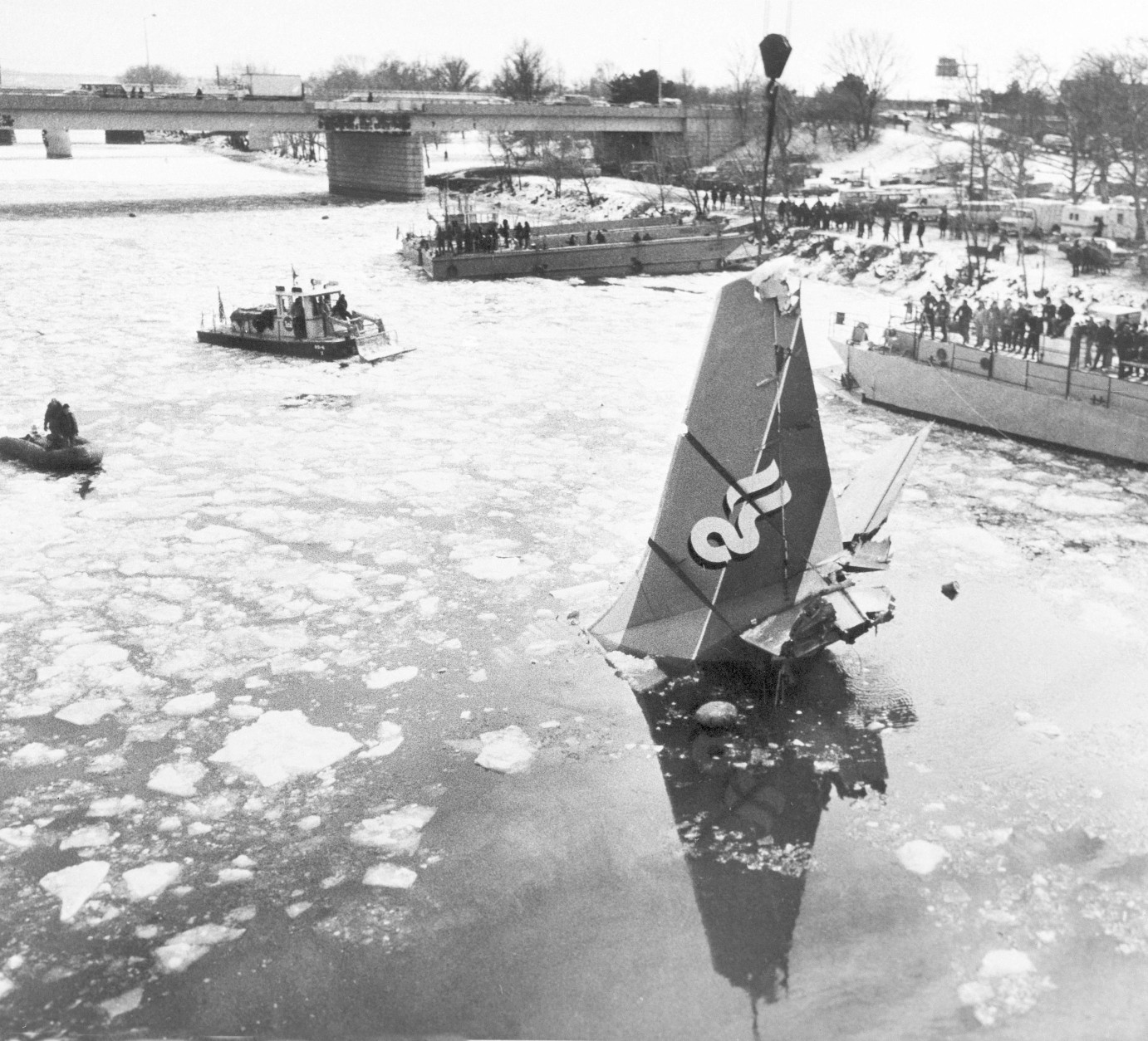 The tail of the Air Florida jet that crashed into the Potomac River in Washington, D.C.,  is hoisted from the water by a crane, Jan. 18, 1982, during salvage efforts. The 14th Street Bridge that the plane hit while taking off from National Airport is pictured in background. (AP Photo)