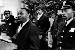 Dr. Martin Luther King Jr., president of the Southern Christian Leadership Conference, is heavily guarded as he speaks to an estimated crowd of 2,500 who braved freezing weather to attend an anti-segregation rally in downtown Hurt Park Sunday Dec. 16, 1963 in Atlanta. Police said the integration leader's life had not been threatened, but the officers were a precautionary measure. (AP Photo)