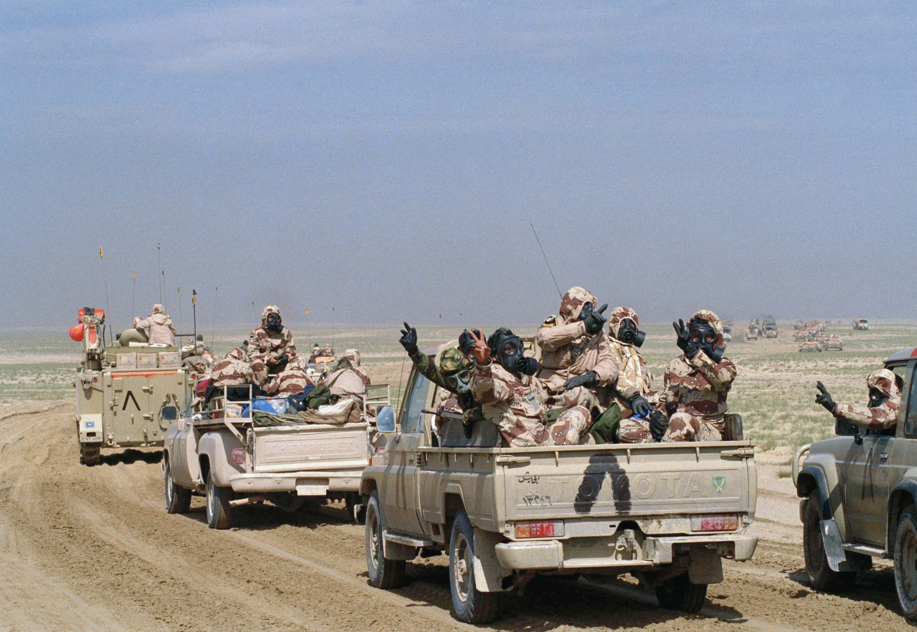 Kuwaiti troops wearing gas masks and protective suits as they roll through southern Kuwait in an armed motor convoy, Sunday, Feb. 24, 1991, the first full day of ground conflict in Operation Desert Storm. Allied troops encountered resistance in some areas, but no use of gas weapons was reported. Inverted "V" painted on vehicles is the allied recognition symbol. (AP Photo/Laurent Rebours)