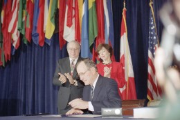 Pres. George H. W. Bush, center, signs the North American Free Trade Agreement during a ceremony at the Organization of American States headquarters, Thursday, Dec. 17, 1992, Washington, D.C. Canadian Amb. Derek Burney and U.S. Trade Representative Carla Hills applaud during the signing. The president predicted an explosion of growth throughout North America as he signed the agreement. (AP Photo/Dennis Cook)