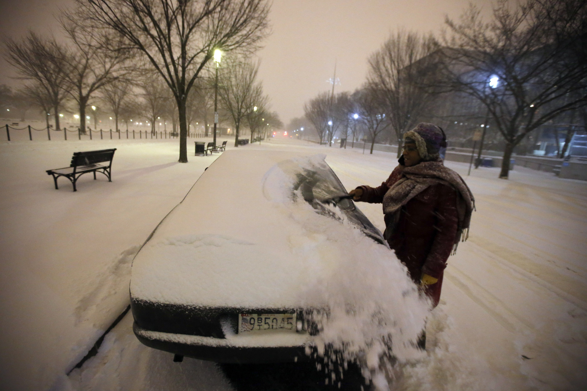 Ndimyake Mwakalyelye cleans off her car after getting off work, as the snow continues to fall, Friday, Jan. 22, 2016 in Washington. (AP Photo/Alex Brandon)