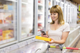 Cheerful young woman texting on mobile phone in supermarket.