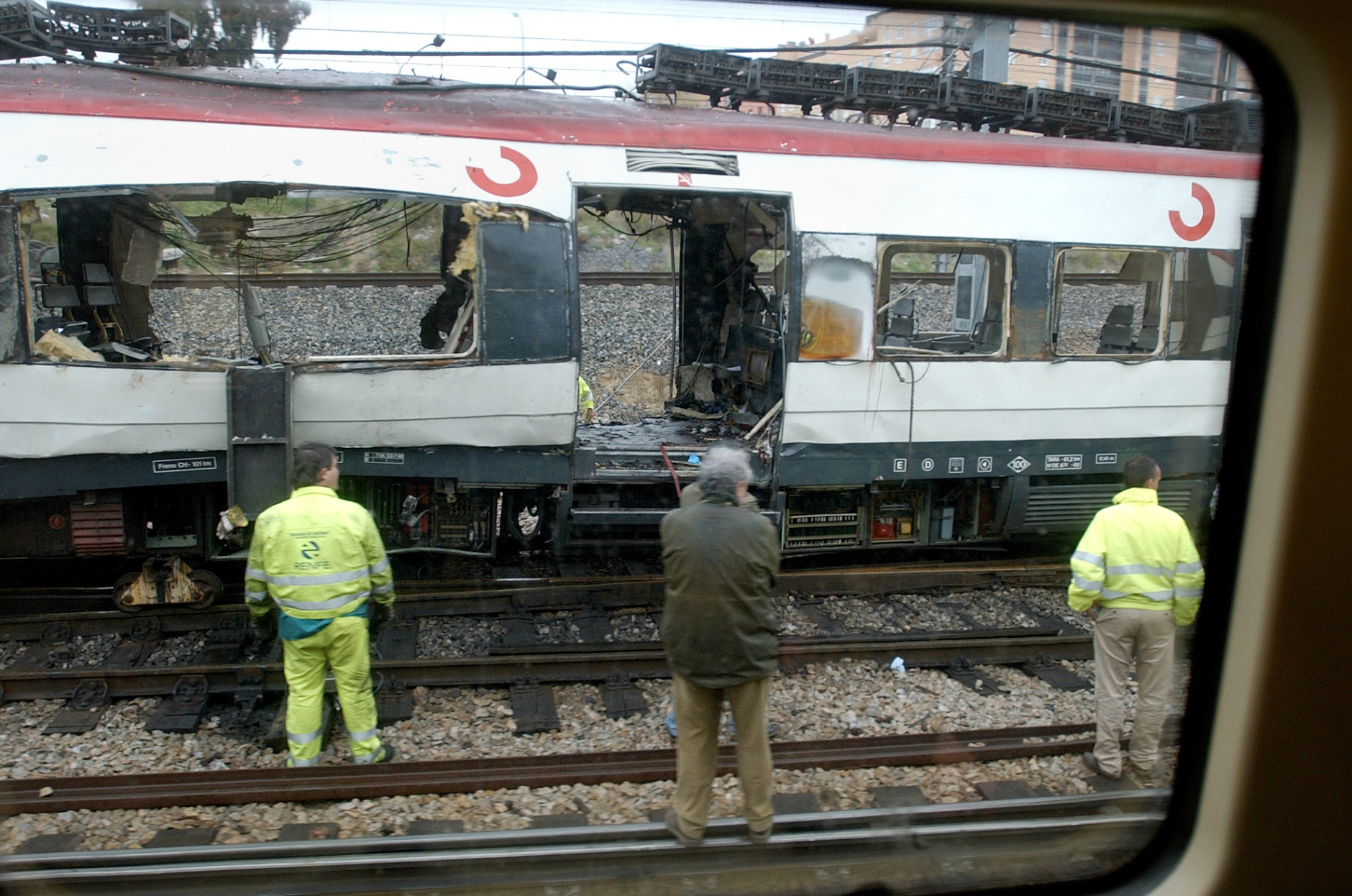 Workers stand next to a bomb damaged passenger train a day after a number of explosions  in Madrid, in this March 12, 2004, file photo. A Spanish judge on Tuesday, April 11, 2006, handed down the first indictments in the Madrid train bombings of 2004, charging 29 people with murder, terrorism or other crimes after a two-year probe. (AP Photo/Peter DeJong)